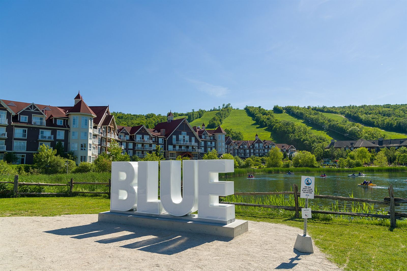Large white BLUE letters by the Mill Pond, with the Village and green ski runs behind