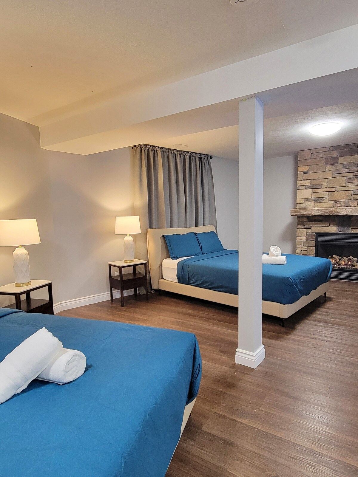Large ground-floor bedroom with two queen beds in teal linens and a stone fireplace