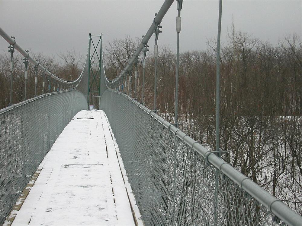 A snow-covered suspension bridge stretching over a winter forest