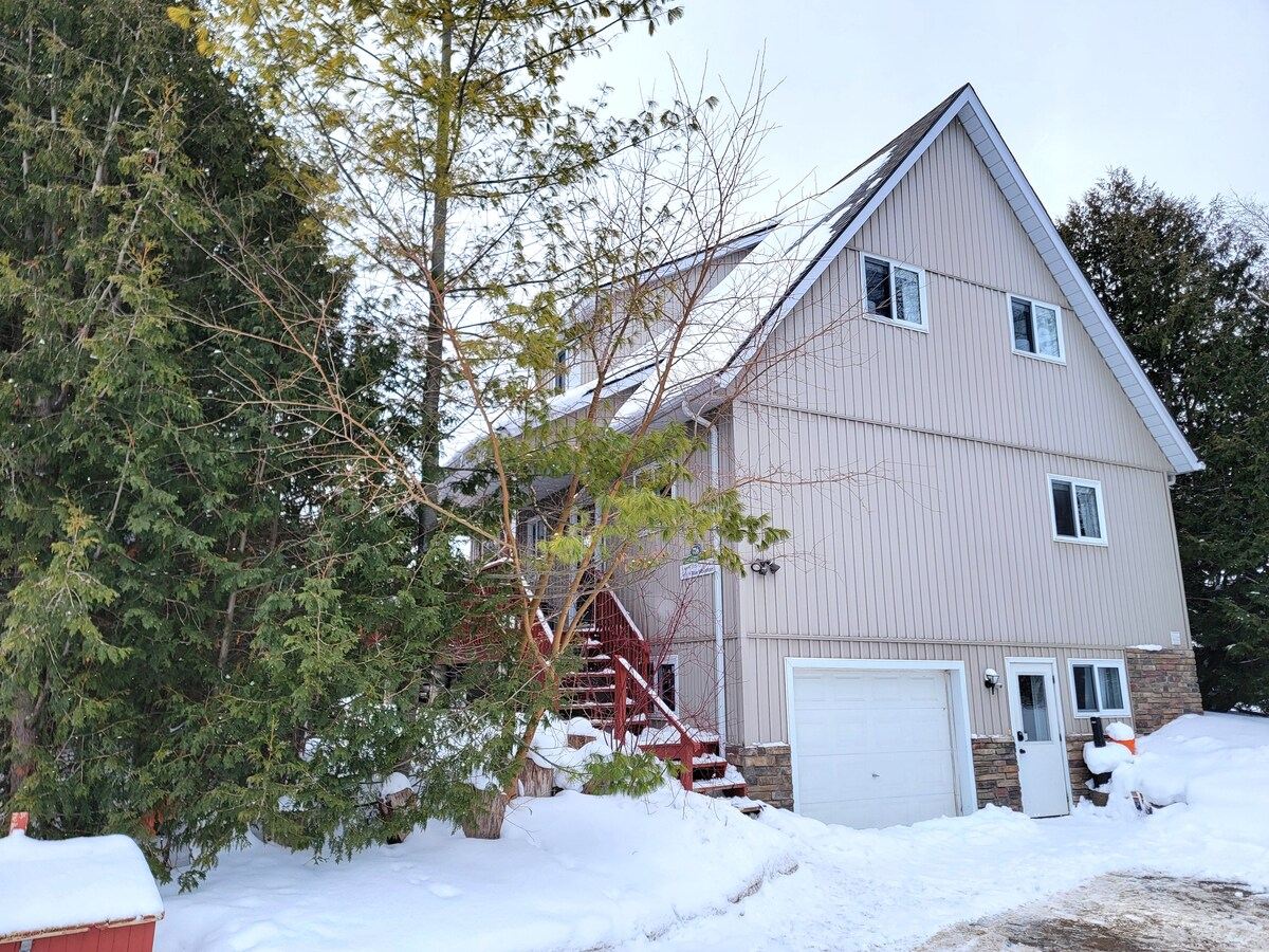 The tall A-frame chalet with snow on the ground and evergreens around it