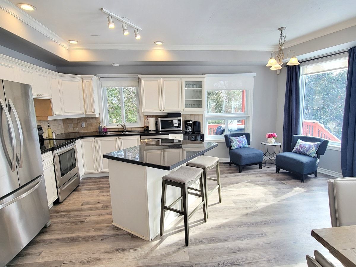 White kitchen with stainless appliances, an island with stools and a coffee corner by the windows