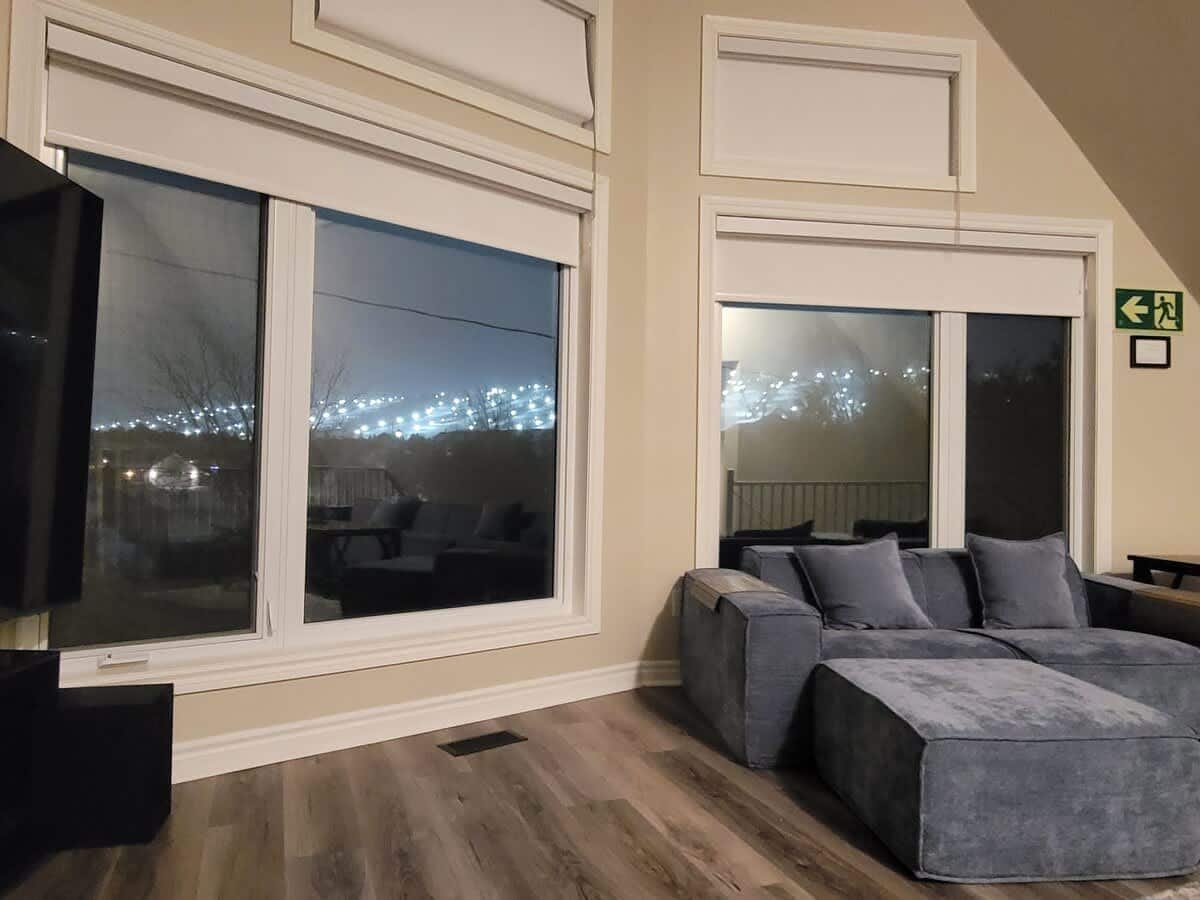 Loft living room at night, a deep sofa beside tall windows with the lit ski runs of Blue Mountain glowing in the distance