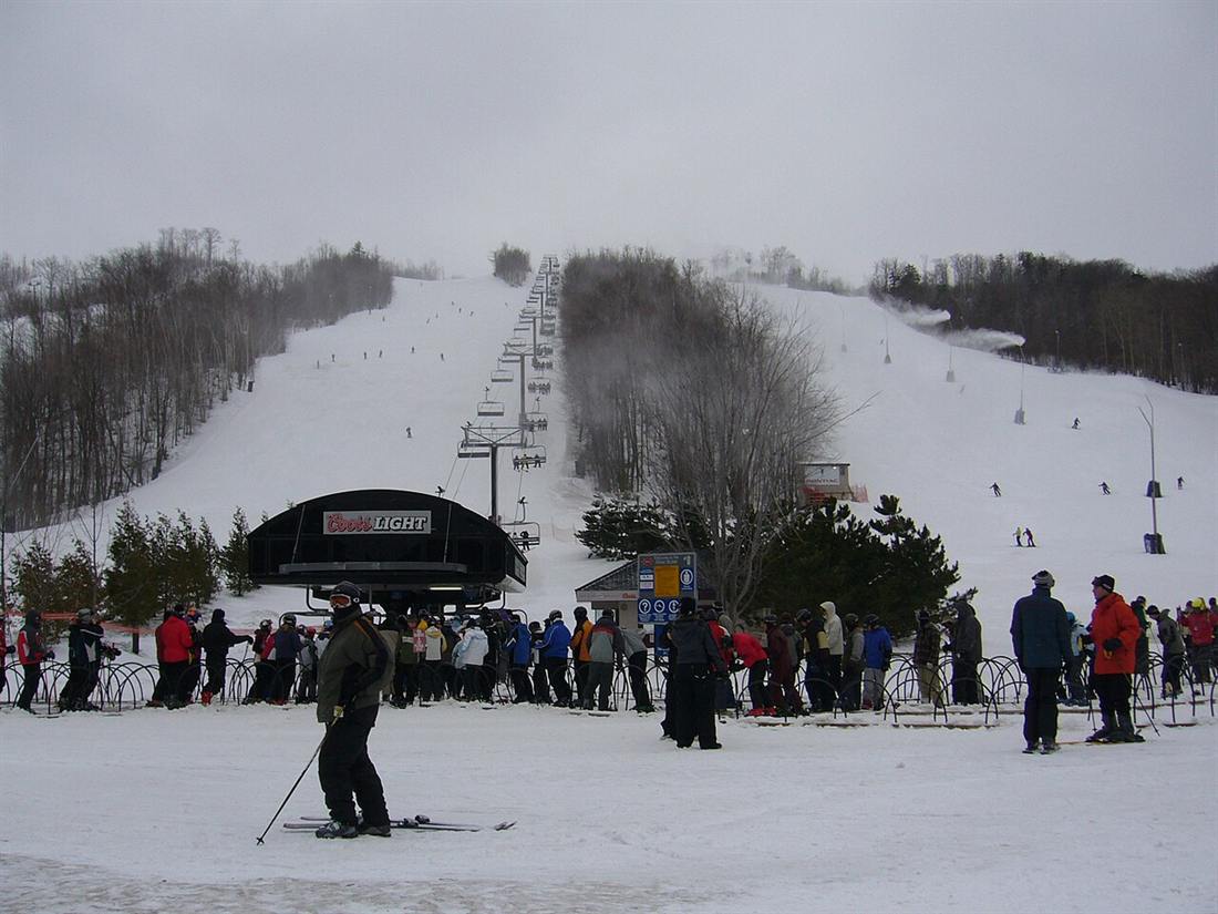 Skiers gathered at the base of a chairlift with snowy runs above